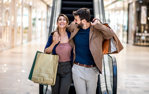 Joven pareja feliz atractiva abrazando, sonriendo y sosteniendo bolsas de compras mientras camina en el centro comercial. photo