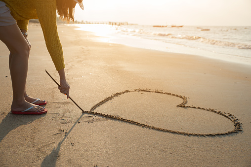 Beautiful woman writing message (heart symbol) on sand beach to her friend or boyfriend.