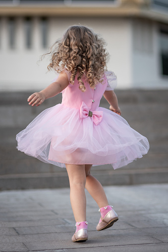 Little girl in pink dress spinning around on the street. Back view