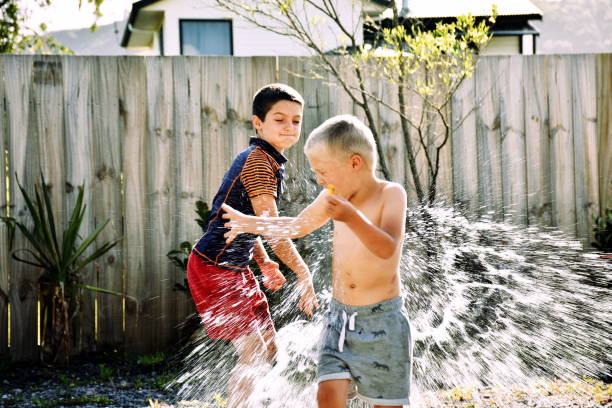 Children Water Bomb Fighting A child throws a water bomb at another child in summer. water balloon stock pictures, royalty-free photos & images