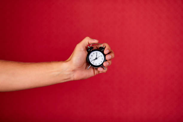 istock Men holding black alarm clock in one hand on red studio background 1277278012