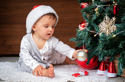 cute baby with Christmas tree. happy child sitting near the christmas tree, reaching for the christmas ornament with interest