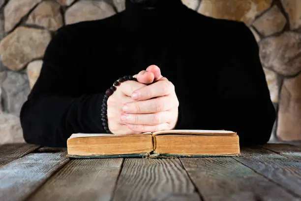 a man in black clothes with a rosary in his hands in front of an open old book the Bible or the Koran, the concept of prayer