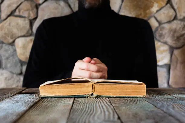 a man in black clothes in front of an open old book the Bible or the Koran, the concept of prayer, study, witchcraft. selective focus