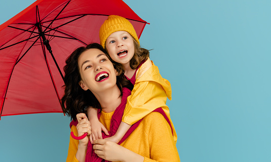 Happy emotional child and mother laughing and hugging. Family with red umbrella on colored teal background.
