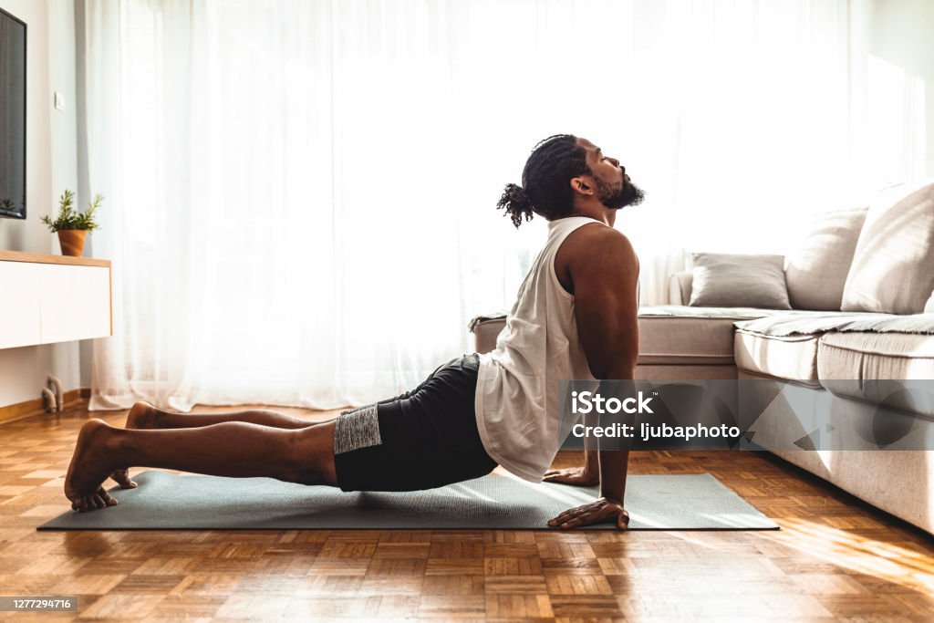 Taking a moment to breathe Indoor shot of handsome young man practicing yoga. Fitness man meditating with his eyes closed while doing cobra pose in living room. Yoga Stock Photo