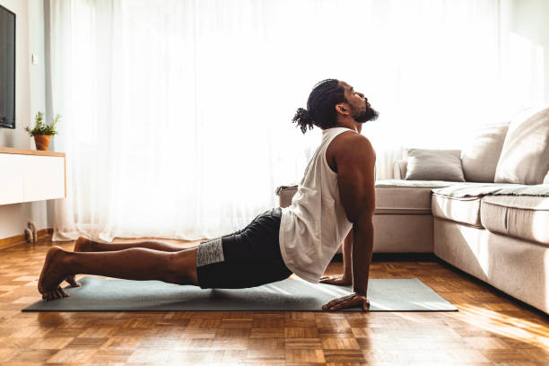 Taking a moment to breathe Indoor shot of handsome young man practicing yoga. Fitness man meditating with his eyes closed while doing cobra pose in living room. exercise mat photos stock pictures, royalty-free photos & images