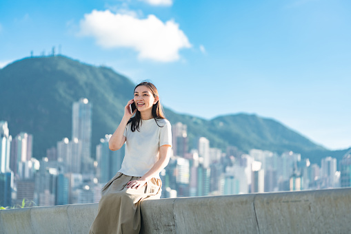 Young Asian Woman Using a Mobile Phone in Hong Kong, overview of the Victoris harbour