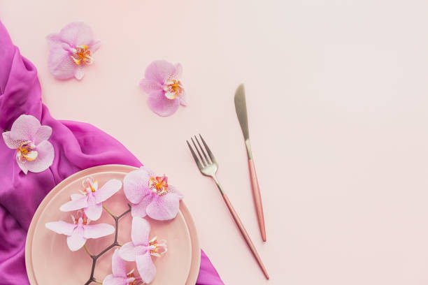 istock Flower and table settings overhead composition on light pink background. Pink ceramic plates, cutlery and perple orchid flowers. Holiday modern table decoration. Romantic date. 1277296737