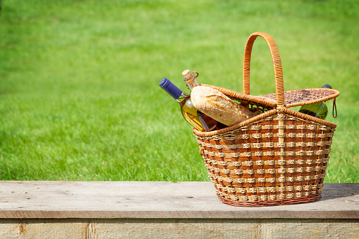 Picnic basket with wine and baguette on garden table. With copy space