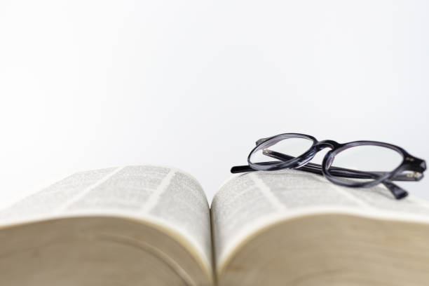 istock Close-up of a folded reading glasses on an open book on a white background 1277302600