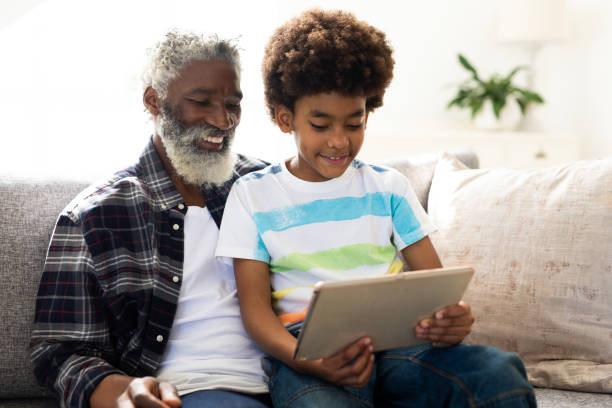 istock Senior man and grandson using digital tablet on couch at home 1277304763