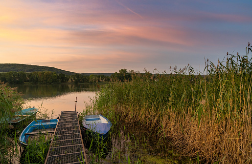 A colorful sunset over lake landscape with small rowboats in the foreground