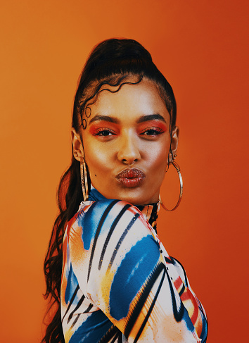 Shot of a young woman posing against a orange background with a trendy hairstyle