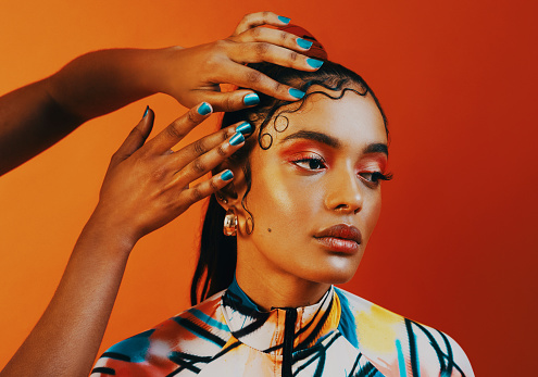 Studio shot of a hairstylist doing a woman's edges against a orange background