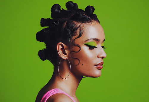Shot of a woman posing against a green background with her bantu knots