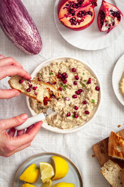 mezze table with baba ganoush dip in the center and a person holding a piece of bread - eggplant dip baba ghanoush middle eastern cuisine imagens e fotografias de stock