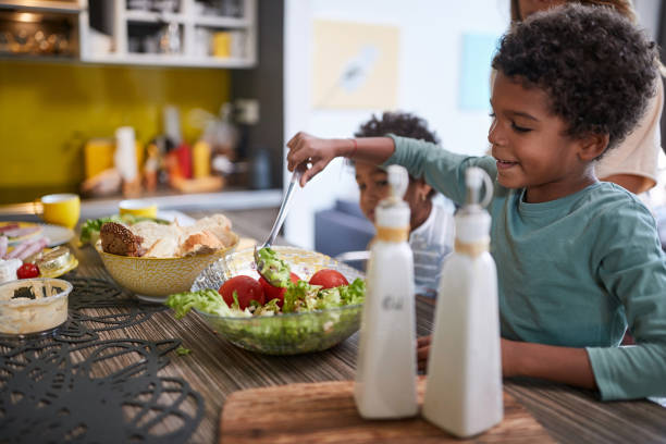 Kid taking salad from bowl in kitchen Little Afro-American kid taking salad from bowl in kitchen boys bowl haircut stock pictures, royalty-free photos & images