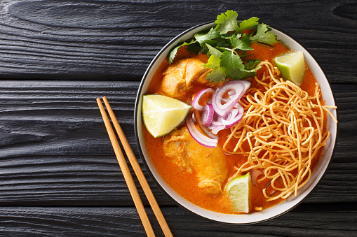 Tasty Khao soi, a noodle soup originating in Thailand, is loaded chicken, shallots, and garlic in a coconut milk-based broth closeup in the bowl on the table. Horizontal top view from above