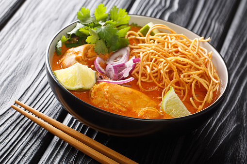 Tasty Khao soi, a noodle soup originating in Thailand, is loaded chicken, shallots, and garlic in a coconut milk-based broth closeup in the bowl on the table. Horizontal