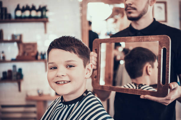 Boy sits in a chair with a new haircut and smiles. stock photo