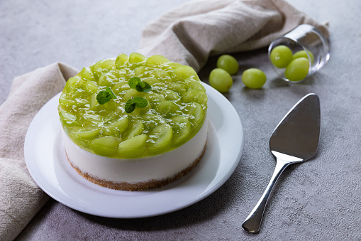 No-bake cheesecake with grapes jelly, decorated with green grapes on a on a gray table