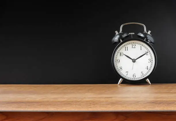 Photo of Retro alarm black clock vintage style on wooden table a black wall background with copy space.