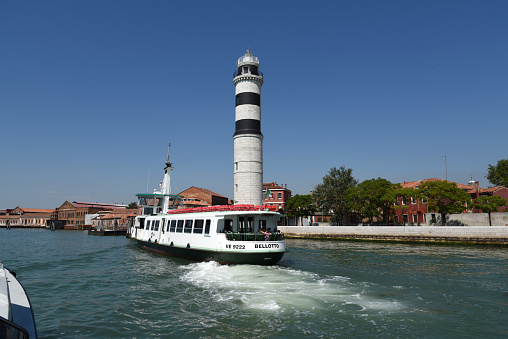 Murano Island near Venice with its beautiful lighthouse and a vapretto waterbus befor it. The image was captured during the worldwide coronavirus pandemic (CVOID19).