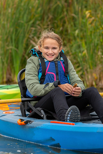 Close-up of a young girl sitting in her blue kayak on the lake. She is smiling at the camera. Taken on an early autumn day in Minnesota, USA.