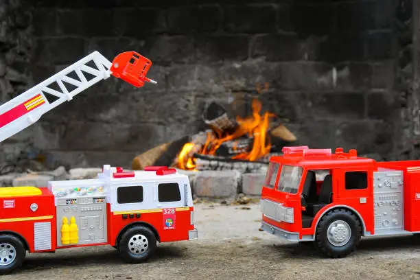Toy red firetrucks "help out" at a real fire in an outdoor fireplace
