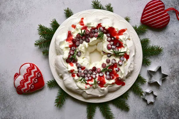 Christmas meringue cake Pavlova with cranberry and rosemary on a light  slate, stone or concrete background. Top view with copy space.
