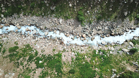 River in the woods. The view from the top. A rushing river among rocks. Green firs and grass grow along the edges. The shadow of the forest falls on the rocks. Flying over the river. Kazakhstan.