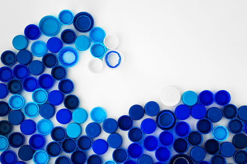 Blue wave from plastic bottle caps on a white background. Concept showing plastic pollution of the ocean. Sorting garbage. Recycling plastic. Space for text.