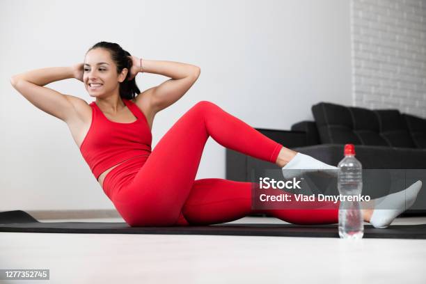 Young Woman In Red Tracksuit Doing Exercise Or Yoga At Home Cheerful Confident Wellbuilt Girl Doing Abs And Legs Exercise On Yoga Mat Holding Hands Behind Head Homie Workout Stock Photo - Download Image Now