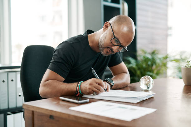 He knows his brand like the back of his hand Shot of a mature businessman filling out paperwork at his desk in a modern office written goals stock pictures, royalty-free photos & images