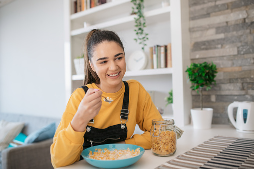 Cheerful Caucasian woman eating cereals for breakfast at home, starting the day healthy and smiling