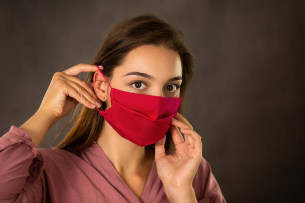 Woman putting on red cloth face mask on dark background