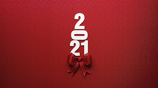 2021 text forming a Christmas tree and is tied with red ribbon on red background. Horizontal composition with copy space. Directly above. Great use for Christmas related gift concepts.