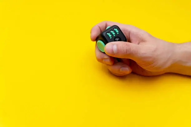 Photo of Antistress fidget in mans right hand on yellow background, close up, copy space