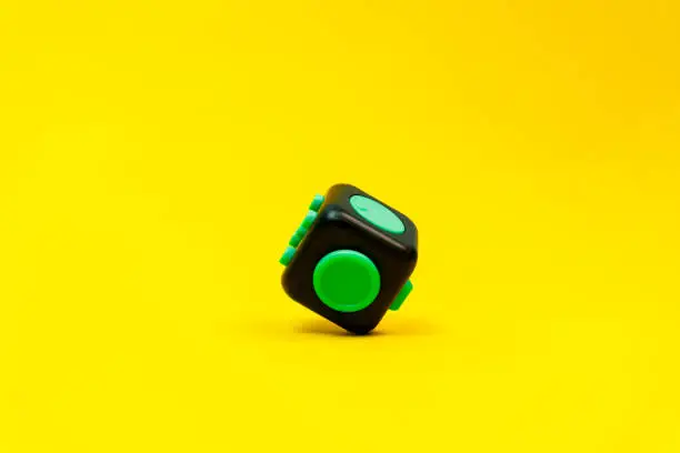 Photo of Closeup of black and green fidget on yellow background, minimal concept, levitation, copyspace.