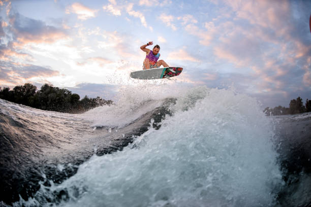 uomo attivo impegnato in sport acquatici estremi sul wakeboard in stile surf. - wakeboarding surfing men vacations foto e immagini stock