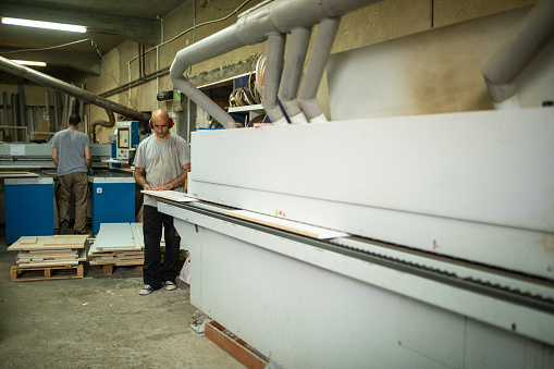 Carpenter working on veneer machine in furniture factory