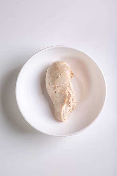 Fresh raw chicken pieces on a wooden cutting board with knife, surrounded by green vegetables and cooking utensils in a home kitchen. Preparing fresh ingredients with reusable food containers, promoting sustainable cooking and zero-waste meal planning at home.
