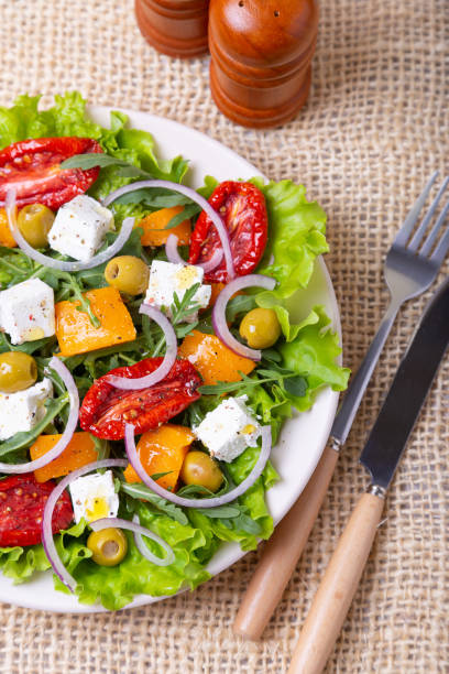 Warm salad with pumpkin, feta cheese, dried tomatoes, olives, arugula and red onion. Warm salad with pumpkin, feta cheese, sun-dried tomatoes, olives, arugula and red onions. Close-up. side salad stock pictures, royalty-free photos & images