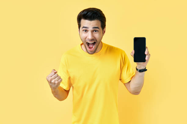 istock Excited screaming man holding mobile phone and looking to camera in yellow studio 1277377462