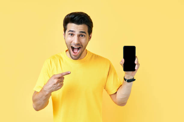 istock Excited screaming man pointing his finger showing mobile phone and looking to camera 1277377470