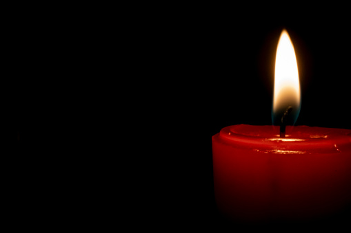 Red lit candle burns with blank copy space on left