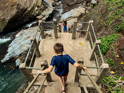 High angle view of two children on holiday walking down concrete steps in the Sambangan Secret Garden near to the Aling Aling waterfall together in Bali, Indonesia.