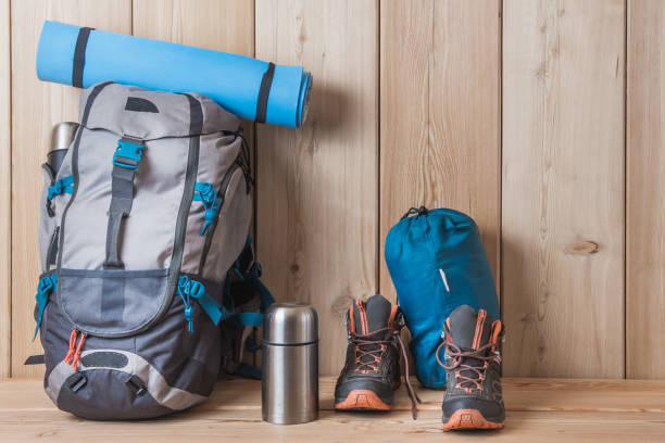 istock Camping equipment, shoes, a backpack and a thermos on a wood background 1277382082
