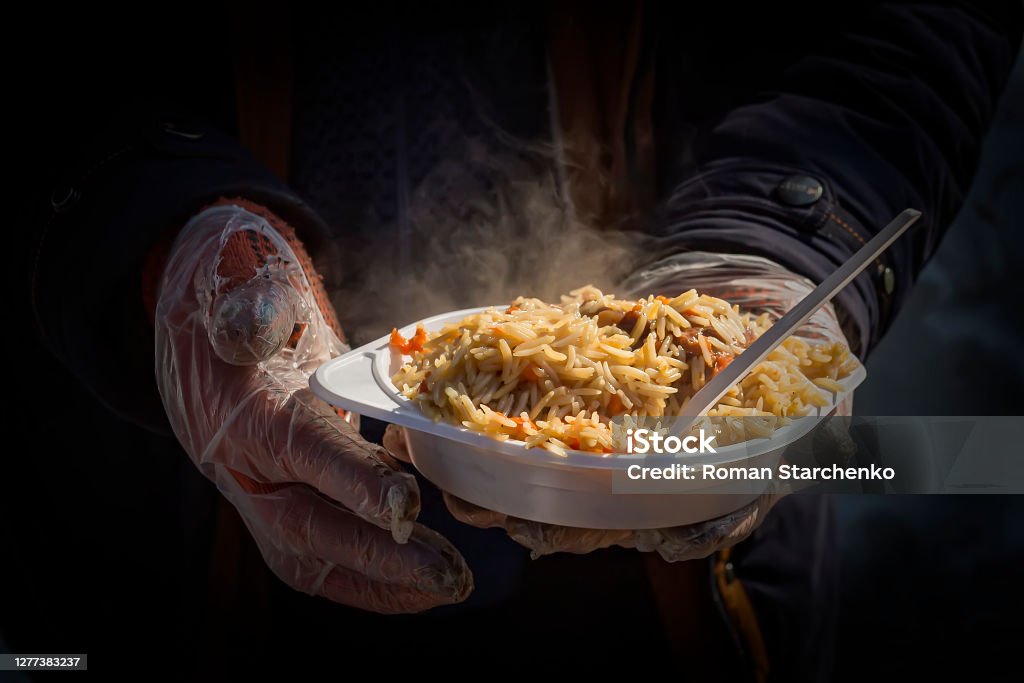 Food for the homeless. Street food. Plate with pilaf in hands Food for the homeless. Street food. Plate with pilaf in hands in disposable gloves. Begging - Social Issue Stock Photo